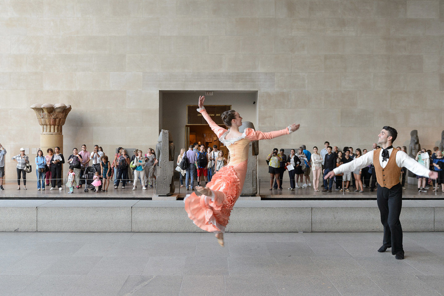 Two dancers perform in the Temple of Dendur gallery; a crowd of spectators appears behind them in the far distance